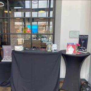 Cocktail table with black linens and the bar setup at an event